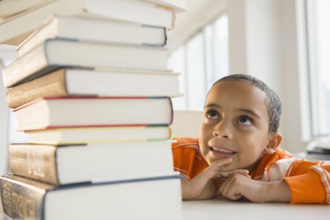 Mixed race boy looking up at stack of books