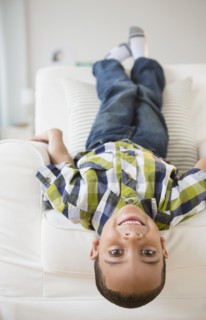 Mixed race boy laying upside-down on armchair