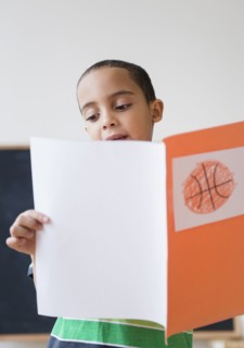 Mixed race boy reading report on basketball in class