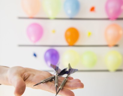 African American woman holding darts by wall of balloons