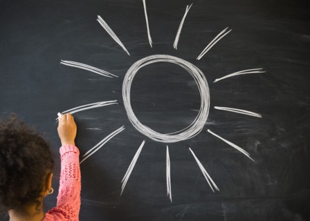 African American girl drawing sun on board in classroom