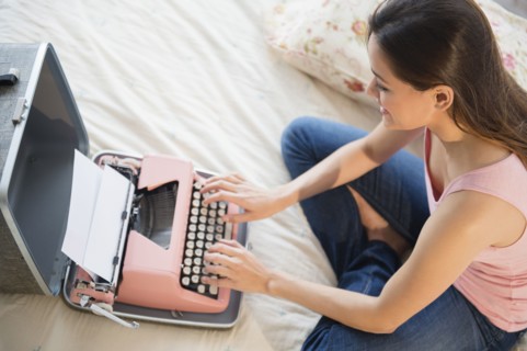 Woman using typewriter on bed
