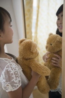 Filipino girl admiring teddy bear in mirror