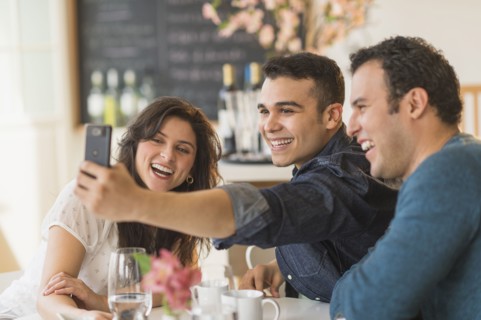 Hispanic friends taking pictures with cell phone in cafe