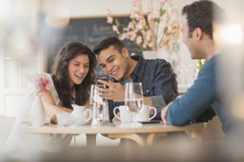 Hispanic friends using cell phone in cafe