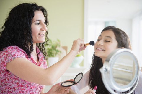Hispanic mother helping daughter apply makeup