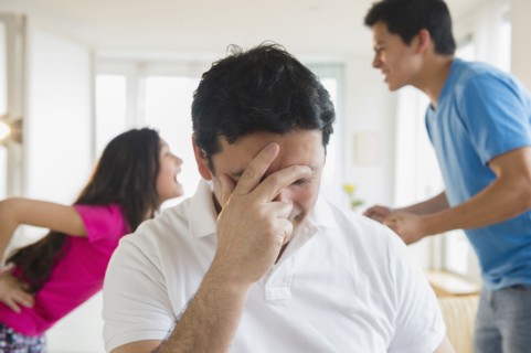 Hispanic father covering his face as children fight behind him