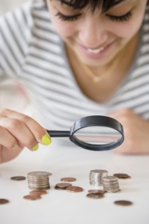 Mixed race woman examining stacks of coins with magnifying glass