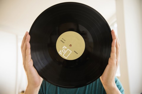 Mixed race man obscuring face with vinyl record