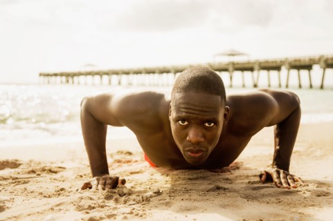 Mixed race man doing push ups on beach
