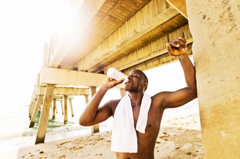 Mixed race man drinking water under pier