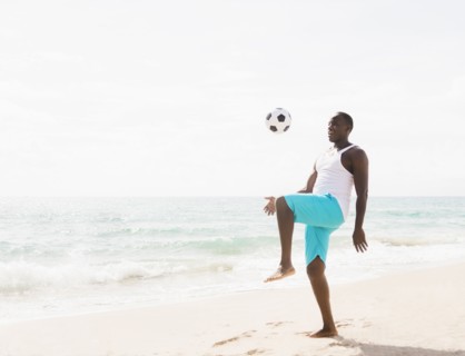 Mixed race man playing with soccer ball on beach