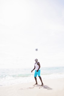 Mixed race man playing with soccer ball on beach