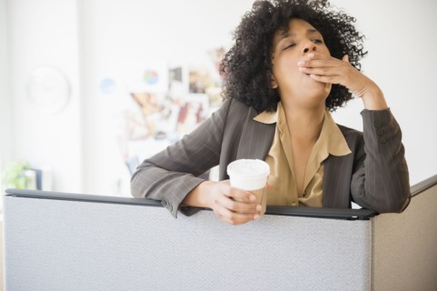 Businesswoman with cup of coffee yawning in cubicle
