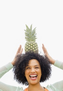 Smiling woman balancing pineapple on head