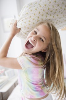 Caucasian girl having pillow fight in bedroom