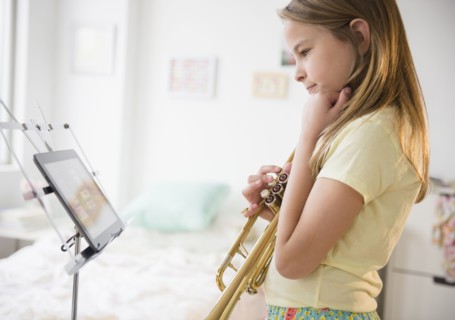 Caucasian girl practicing trumpet with digital tablet