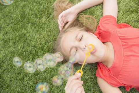 Caucasian girl blowing bubbles on grassy lawn