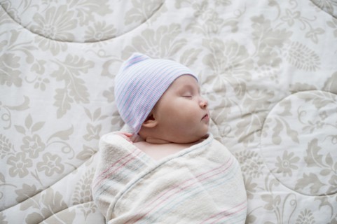Swaddled Asian baby sleeping on bed