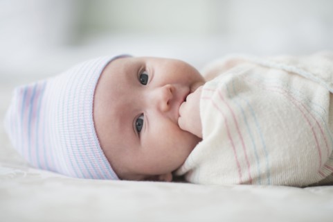 Swaddled Asian baby biting fingers on bed