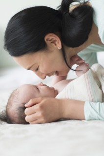 Asian mother holding baby on bed