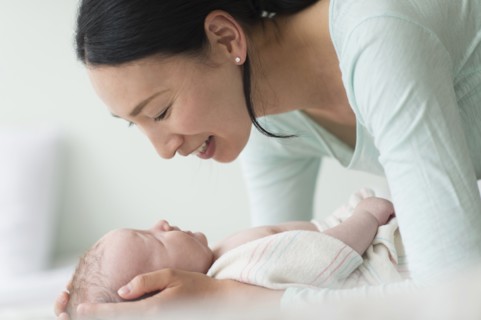 Asian mother holding baby on bed