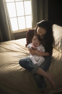 Asian mother holding baby on bed