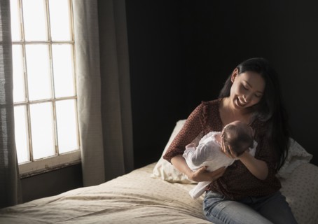Asian mother holding baby on bed
