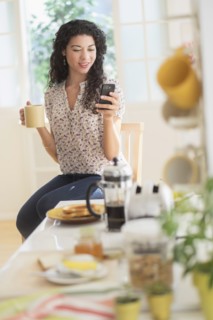 Mixed race woman using cell phone in kitchen