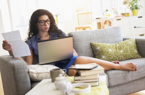 Mixed race woman paying bills on laptop on sofa