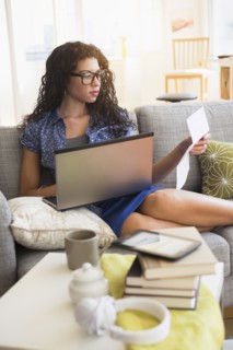 Mixed race woman paying bills on laptop on sofa