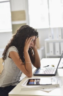 Frustrated mixed race businesswoman working on laptop at desk in office
