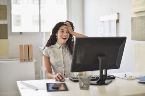 Mixed race businesswoman gasping at computer at desk in office