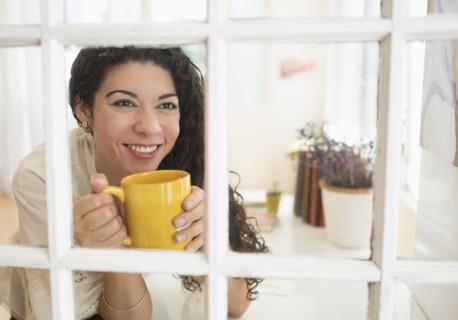 Mixed race woman drinking cup of coffee near window