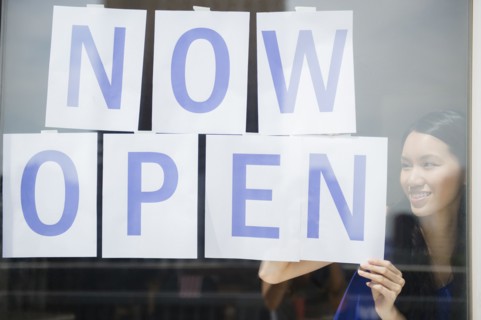 Woman hanging now open sign in store window