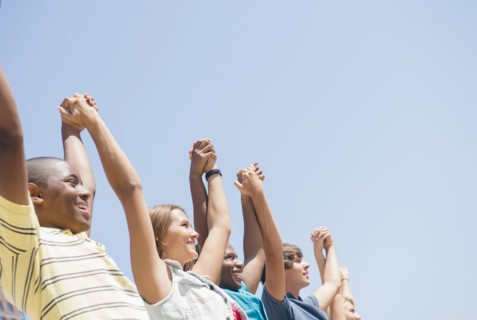 Low angle view of teenagers holding hands under blue sky