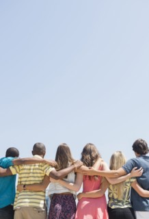 Rear view of teenagers hugging under blue sky