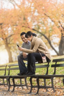 Couple using cell phone on park bench