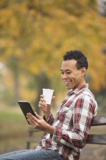 Mixed race man using digital tablet on park bench