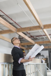 Korean architect holding blueprints and examining ceiling