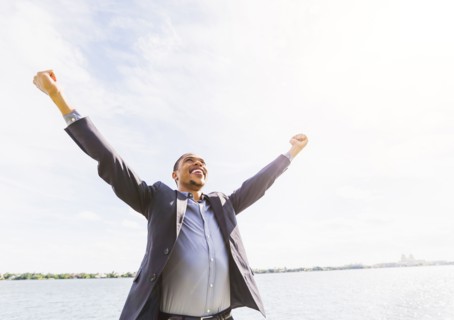 Black businessman cheering with arms outstretched outdoors