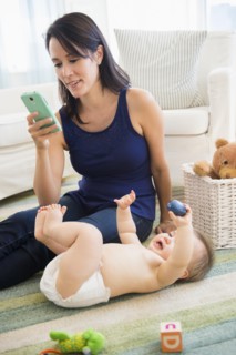 Mixed race mother using cell phone with baby on floor