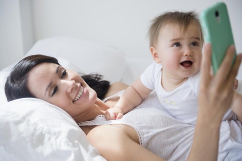 Mixed race mother playing with baby and cell phone on bed