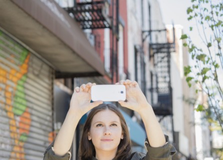 Caucasian woman taking cell phone photograph on urban sidewalk