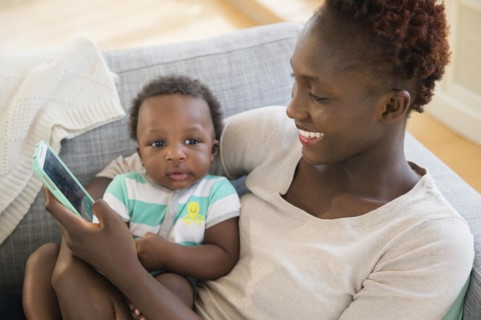 Black mother and son using cell phone on sofa