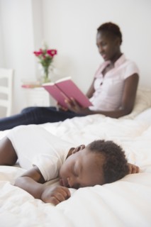 Black mother reading near sleeping baby boy