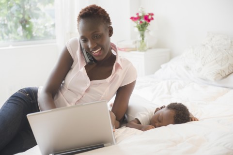 Black mother using laptop near sleeping baby boy