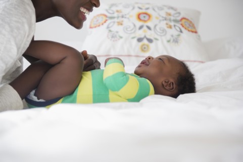 Black mother playing with baby boy on bed