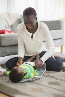Black mother changing diaper of baby boy in living room