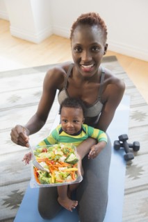 Black mother holding baby boy and eating salad